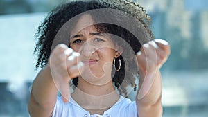 Young beautiful African American woman holds out hands, gives thumbs down gesture of frustration and disgust. Girl