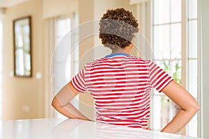 Young beautiful african american woman at home standing backwards looking away with arms on body