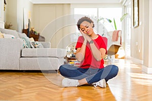 Young beautiful african american woman sitting on the floor at home sleeping tired dreaming and posing with hands together while