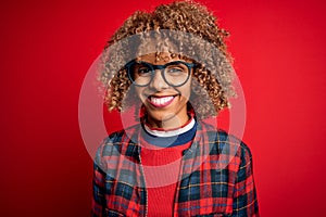 Young beautiful african american woman wearing casual shirt and glasses over red background with a happy and cool smile on face