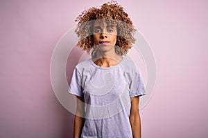 Young beautiful african american woman wearing casual t-shirt standing over pink background with serious expression on face