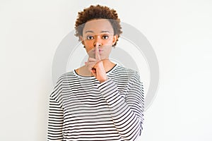 Young beautiful african american woman wearing stripes sweater over white background asking to be quiet with finger on lips