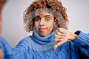 Young beautiful african american woman wearing turtleneck sweater making selfie by camera with angry face, negative sign showing