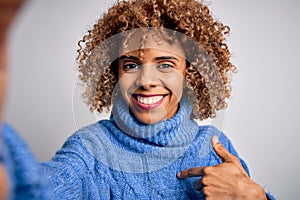 Young beautiful african american woman wearing turtleneck sweater making selfie by camera with surprise face pointing finger to