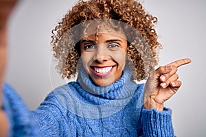 Young beautiful african american woman wearing turtleneck sweater making selfie by camera very happy pointing with hand and finger