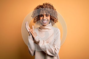 Young beautiful african american woman wearing turtleneck sweater over yellow background clapping and applauding happy and joyful,