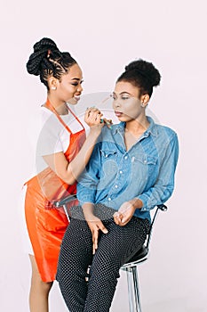 Young beautiful African American woman applying professional make-up by African make-up artist. Studio shoot