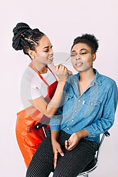 Young beautiful African American woman applying professional make-up by African make-up artist. Studio shoot