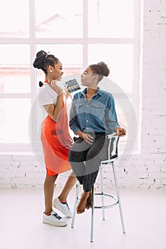 Young beautiful African American woman applying professional make-up by African make-up artist. Studio shoot