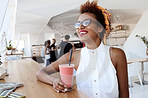Young beautiful african girl drinking smoothie smiling resting in cafe.