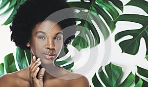 Young and beautiful African woman with perfect smooth skin in tropical leaves