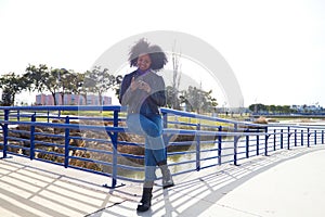 Young, beautiful Afro-American woman with mobile phone shopping online, checking her email and social networks in the park. The