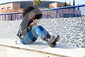 Young and beautiful Afro-American woman sitting in the park while playing with her small breed dog. The woman is wearing casual