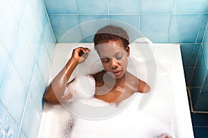 Young and beautiful Afro American woman takes a bubble bath in the bathtub. Beauty and hygiene concept