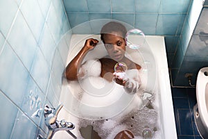 Young and beautiful Afro American woman takes a bubble bath in the bathtub. Beauty and hygiene concept