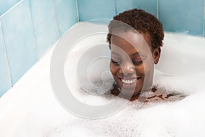 Young and beautiful Afro American woman takes a bubble bath in the bathtub. Beauty and hygiene concept