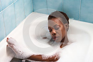 Young and beautiful Afro American woman takes a bubble bath in the bathtub. Beauty and hygiene concept