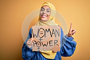 Young beautiful arab woman wearing islamic hijab holding banner with women power message surprised with an idea or question