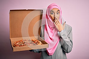 Young beautiful arab woman wearing pink muslim hijab holding delivery box with Italian pizza cover mouth with hand shocked with