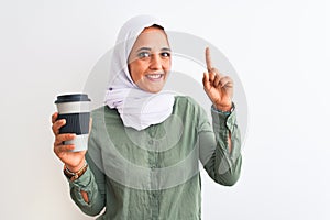 Young beautiful Arab woman wearing traditional Muslim hijab drinking a coffee surprised with an idea or question pointing finger