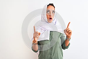 Young beautiful Arab woman wearing traditional Muslim hijab over isolated background amazed and surprised looking up and pointing