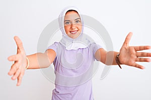 Young beautiful arabian girl wearing hijab standing over isolated white background looking at the camera smiling with open arms