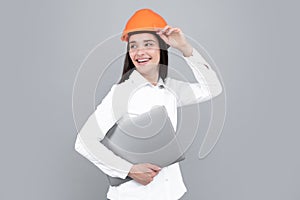 Young beautiful architect woman in hard hat helmet hold laptop computer over gray background. Female builder in helmet