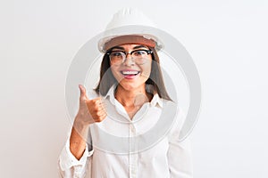 Young beautiful architect woman wearing helmet and glasses over isolated white background doing happy thumbs up gesture with hand