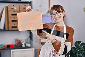 Young beautiful artist woman holding wooden case smiling happy pointing with hand and finger