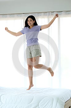 Young beautiful Asia woman wake up and feeling relaxing in the morning. She is jumpping on her bed photo