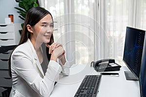 Young beautiful Asian businesswoman looking on pc to analyze stock. Stratagem.