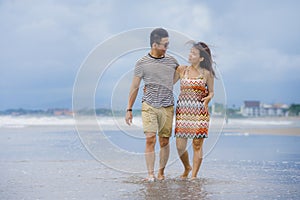 young beautiful and Asian Chinese romantic couple walking together embracing on the beach happy in love enjoying holidays