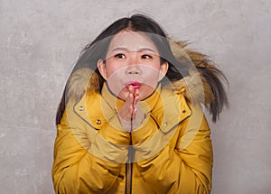 Young beautiful Asian Chinese woman feeling cold and chilly freezing feeling cold in Winter weather wearing yellow jacket with fur