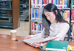Young beautiful Asian female student portrait sitting and concentrate studying or reading textbook in university library for exams