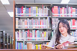 Young beautiful Asian female student portrait sitting and concentrate studying or reading textbook in university library for exams