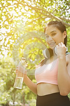 young beautiful asian fitness athlete woman holding drinking water after work out exercising at summer green park.