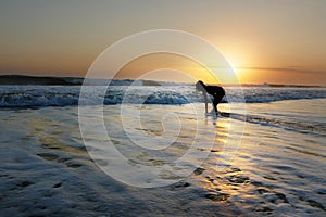 Young beautiful Asian girl alone at sea shore looking at orange sky sunset over ocean