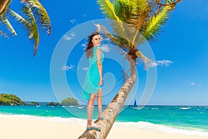 Young beautiful Asian girl with coconut on the palm tree on a tropical beach