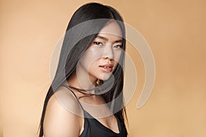 A young beautiful asian girl dressed in a black dress with natural makeup and shiny hair in the wind stands on a beige