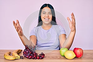 Young beautiful asian girl eating fresh and healthy fruit looking at the camera smiling with open arms for hug