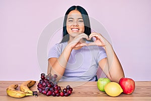 Young beautiful asian girl eating fresh and healthy fruit smiling in love doing heart symbol shape with hands