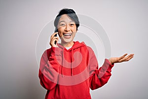 Young beautiful asian girl having conversation talking on the smartphone over white background very happy and excited, winner