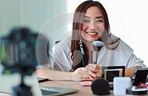 Young and beautiful Asian girl shows various face brushes to camera with smile and happy during broadcast video recording about