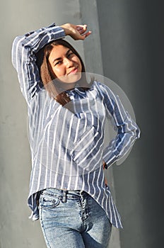 Young beautiful asian girl stands near the wall and posing and she dressed a striped shirt