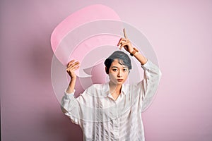 Young beautiful asian girl talking holding speech bubble over isolated pink background with a confident expression on smart face