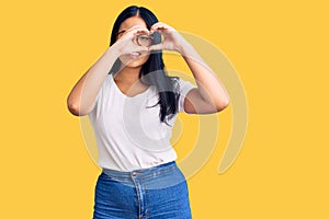 Young beautiful asian girl wearing casual clothes and glasses doing heart shape with hand and fingers smiling looking through sign