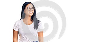 Young beautiful asian girl wearing casual clothes and glasses looking away to side with smile on face, natural expression