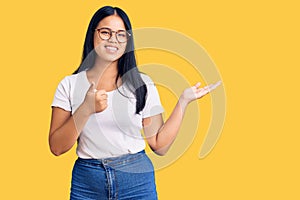 Young beautiful asian girl wearing casual clothes and glasses showing palm hand and doing ok gesture with thumbs up, smiling happy