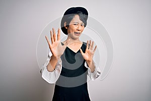 Young beautiful asian girl wearing casual dress and hat standing over isolated white background afraid and terrified with fear