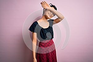 Young beautiful asian girl wearing casual dress standing over isolated pink background covering eyes with arm smiling cheerful and